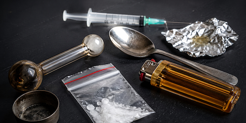 Drug paraphernalia items including pipe, syringe, and packaging materials displayed on a dark surface representing evidence in Tennessee drug-related cases
